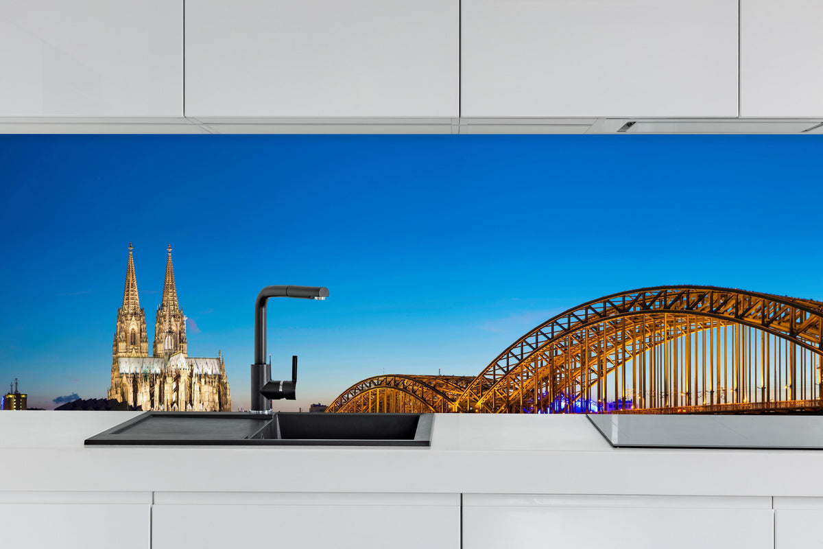 Küche - Hohenzollern Brücke Köln in der Nacht hinter weißen Hochglanz-Küchenregalen und schwarzem Wasserhahn