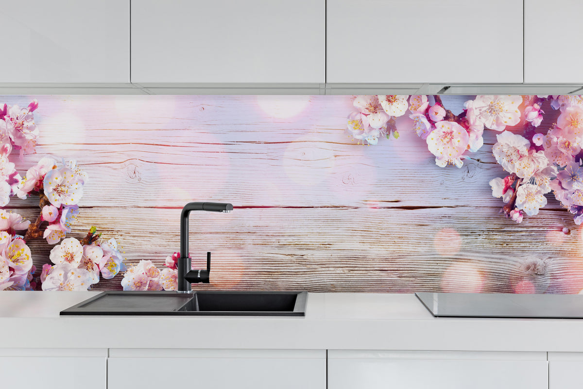 Küche - Rosa Blüten auf Holzplatte hinter weißen Hochglanz-Küchenregalen und schwarzem Wasserhahn