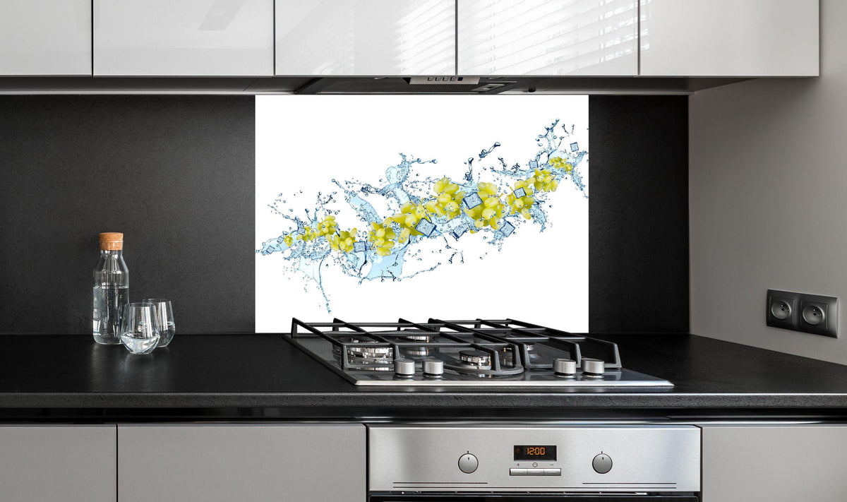 Spritzschutz - Gelbe Trauben mit dynamischem Wasser Splash hinter einem Cerankochfeld zwischen Holz-Kochutensilien
