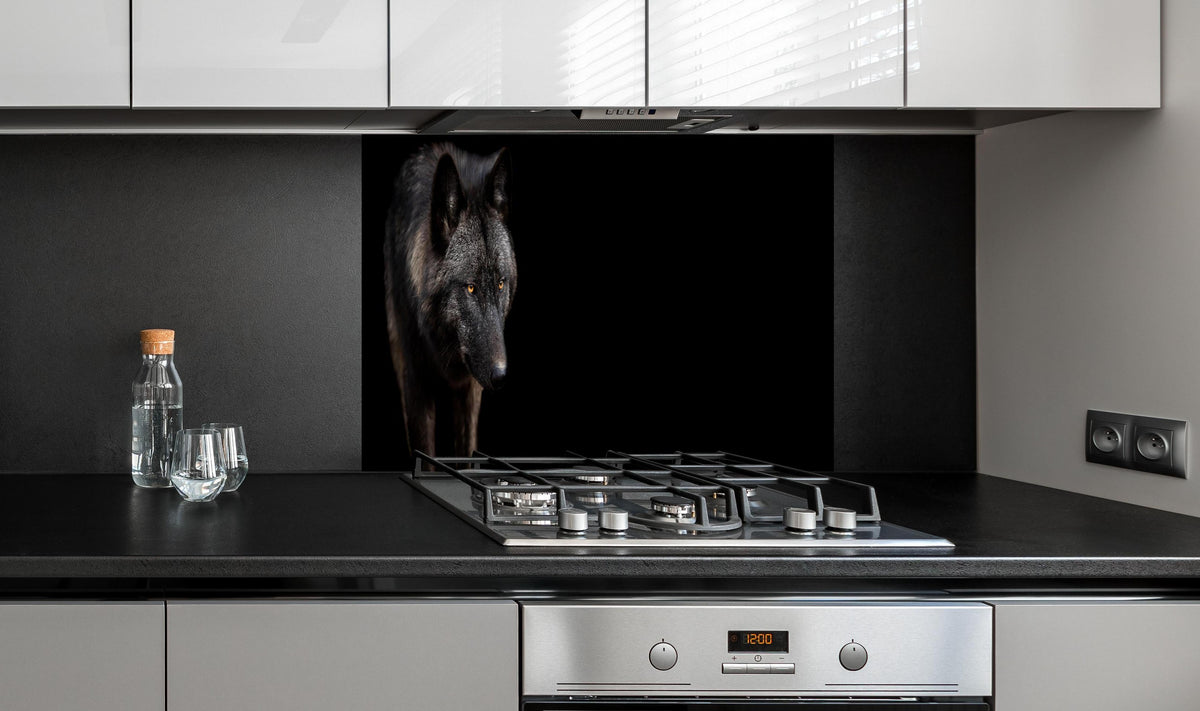 Spritzschutz - Schwarzer Wolf auf schwarzem Hintergrund hinter einem Cerankochfeld zwischen Holz-Kochutensilien
