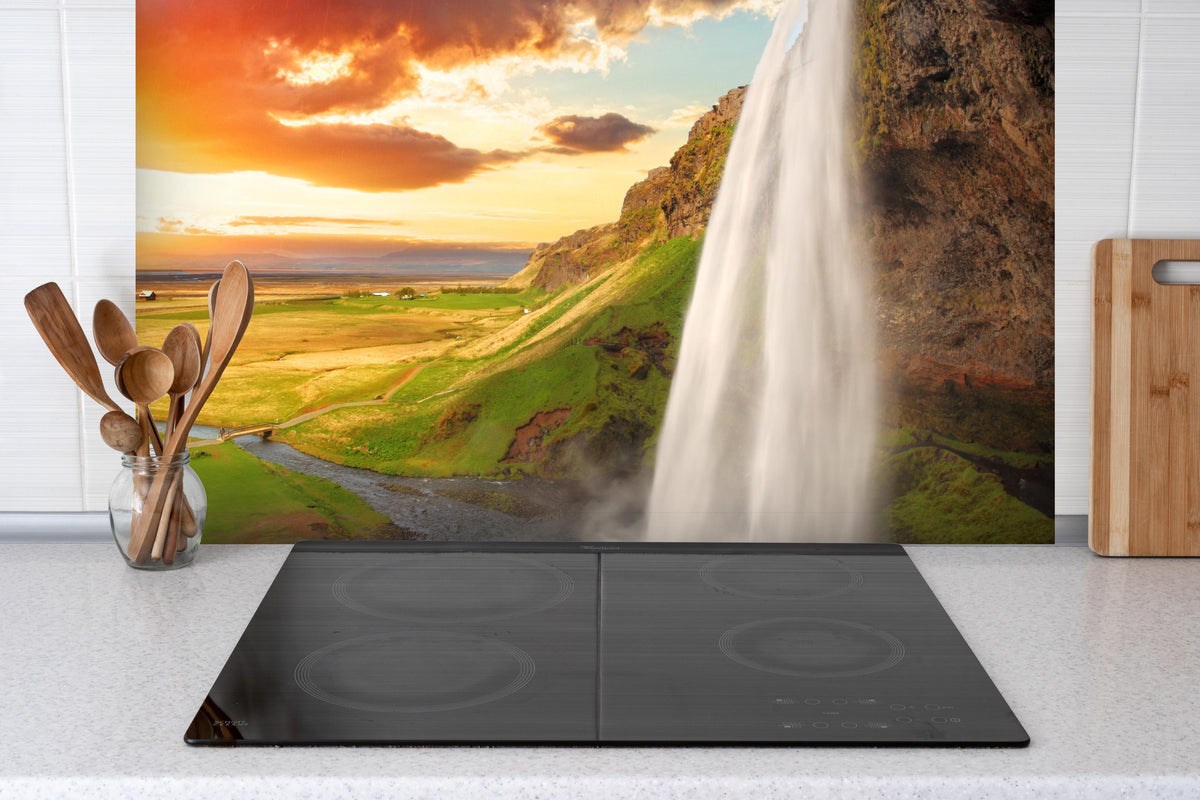 Spritzschutz -  Seljalandsfoss Wasserfall bei Sonnenuntergang hinter einem Cerankochfeld zwischen Holz-Kochutensilien
