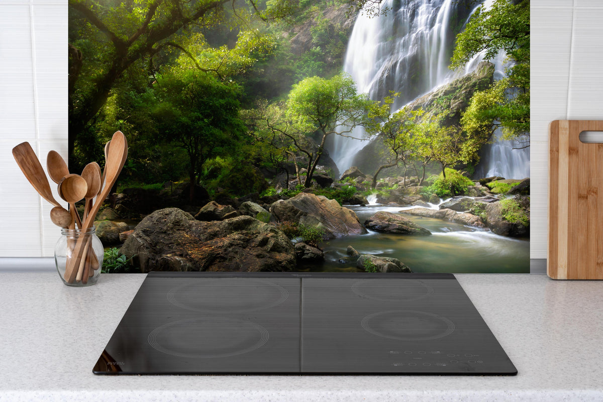 Spritzschutz - Bergbach und Wasserfall in Thailand hinter einem Cerankochfeld zwischen Holz-Kochutensilien
