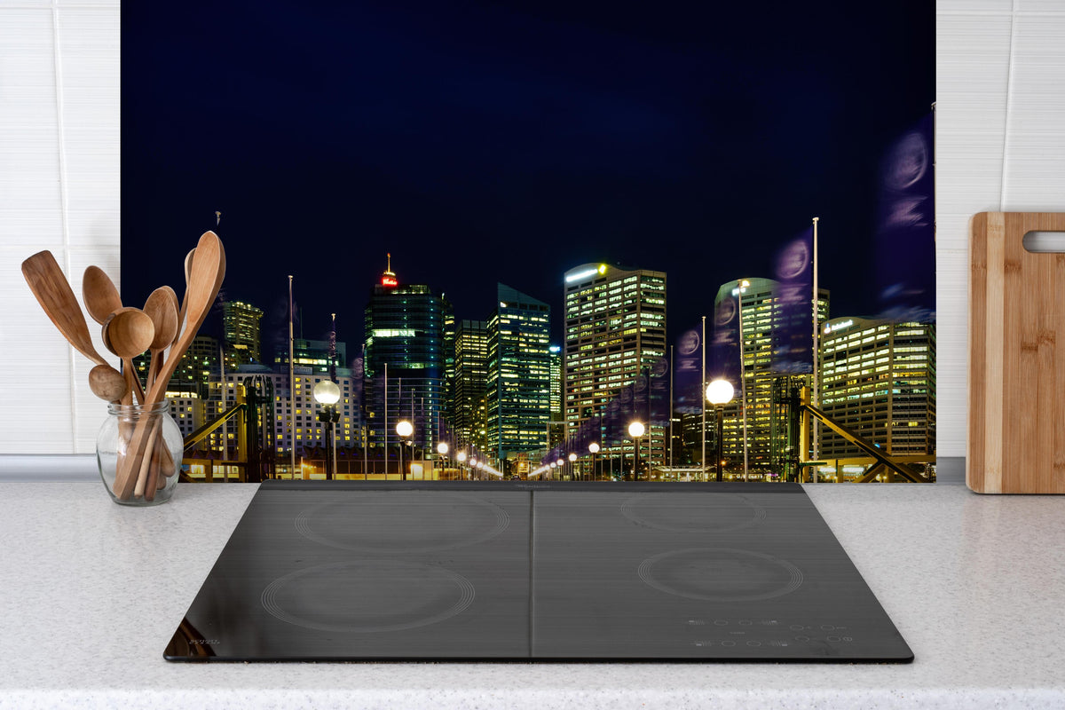 Spritzschutz - Darling Harbour bei Nacht hinter einem Cerankochfeld zwischen Holz-Kochutensilien
