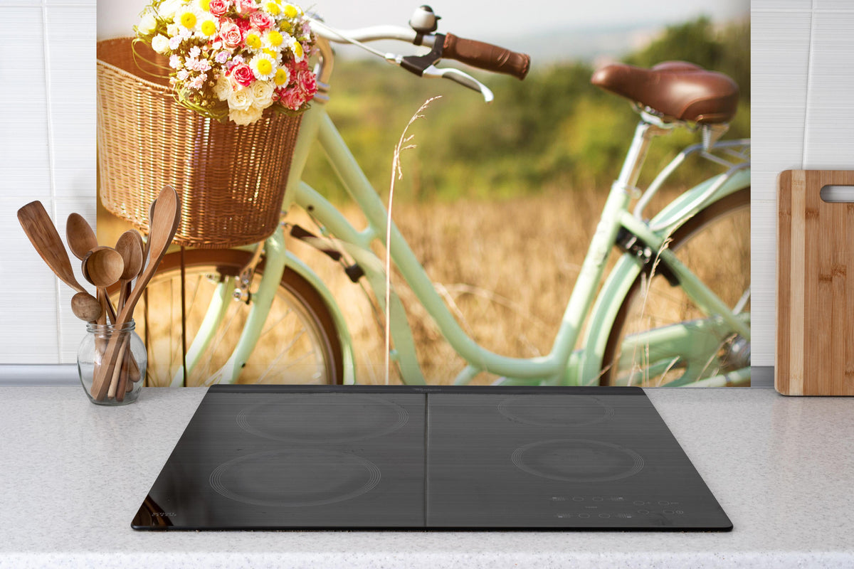 Spritzschutz - Fahrrad mit Blumenkorb auf Wiese  hinter einem Cerankochfeld zwischen Holz-Kochutensilien
