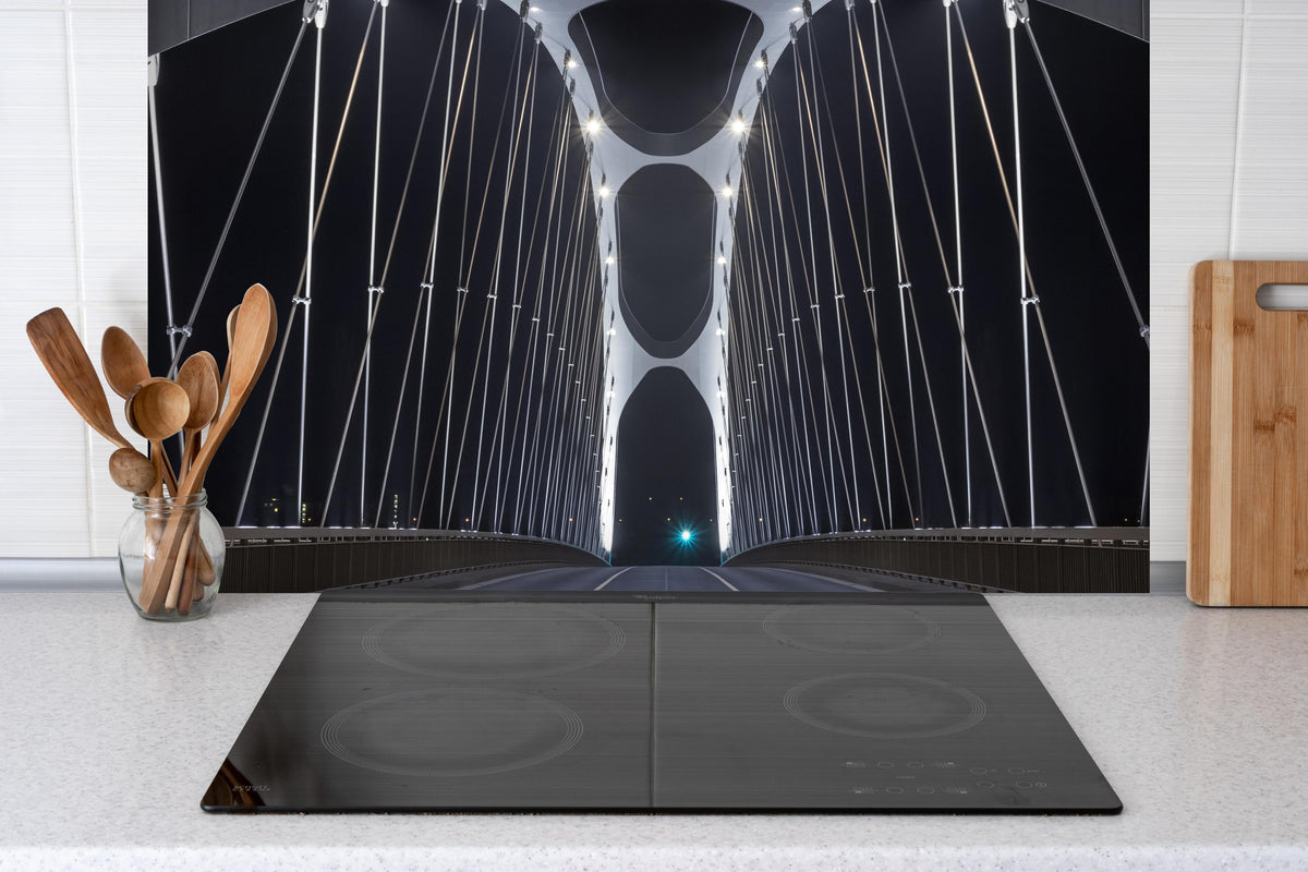 Spritzschutz - Frankfurter Bogenbrücke bei Nacht hinter einem Cerankochfeld zwischen Holz-Kochutensilien
