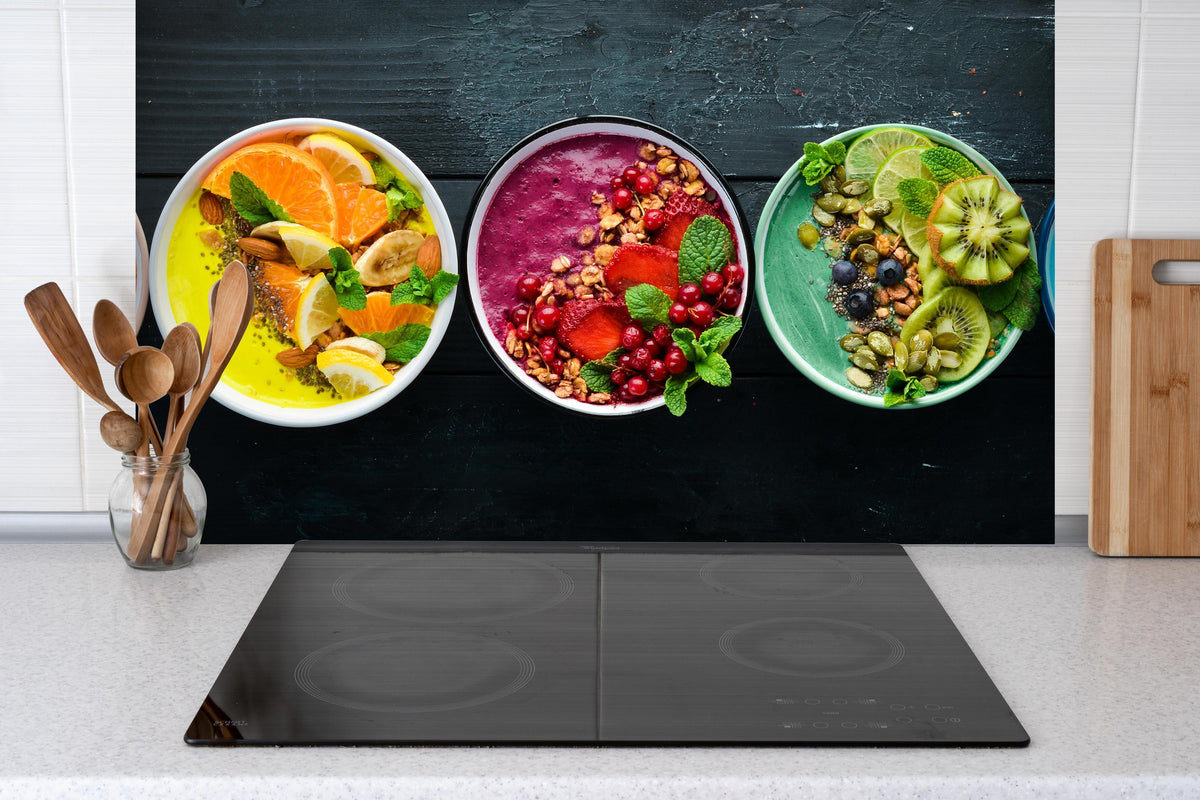 Spritzschutz - Leckere Frucht-Joghurt-Bowls hinter einem Cerankochfeld zwischen Holz-Kochutensilien
