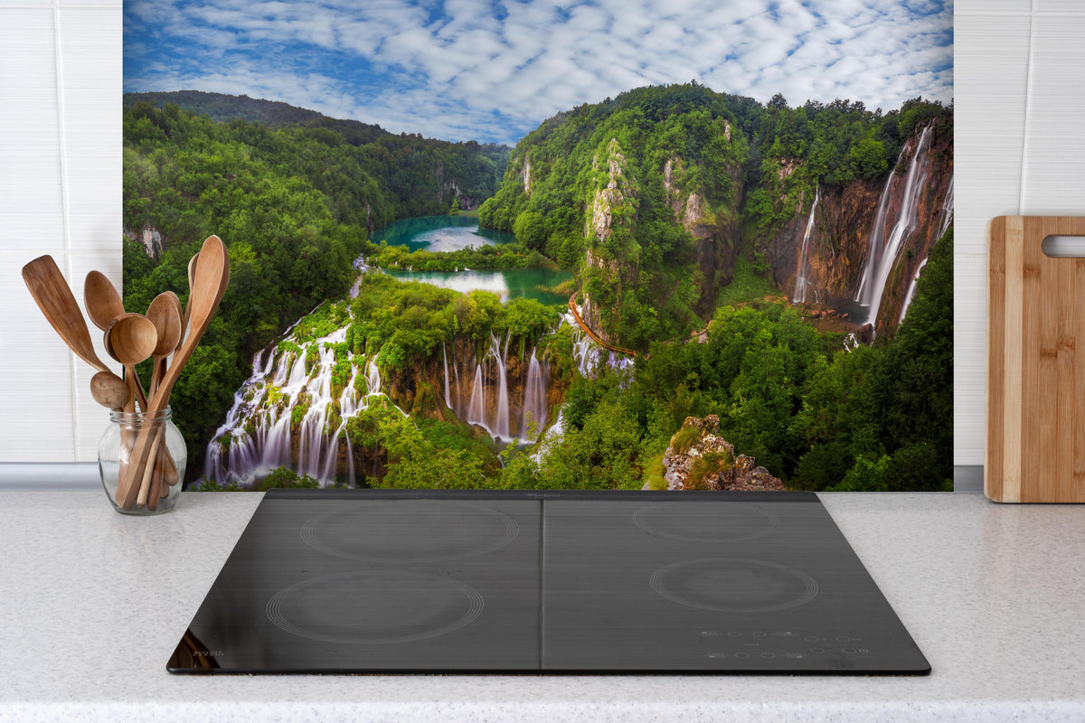 Spritzschutz - Multi-Wasserfall - Landschaft hinter einem Cerankochfeld zwischen Holz-Kochutensilien
