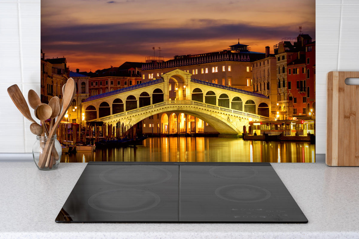 Spritzschutz - Rialtobrücke in Venedig - Dämmerung hinter einem Cerankochfeld zwischen Holz-Kochutensilien
