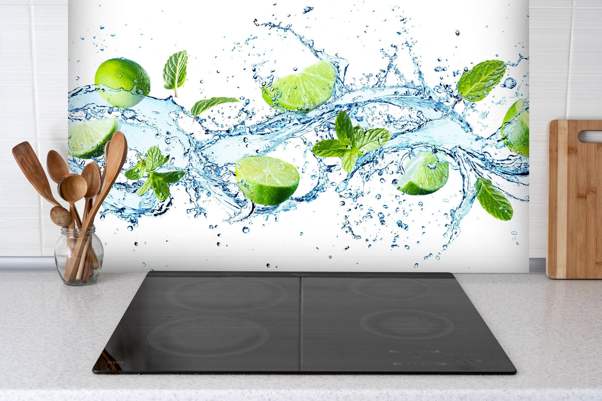 Spritzschutz - Wasserspritzer mit Minzblättern und Limettenspalten hinter einem Cerankochfeld zwischen Holz-Kochutensilien
