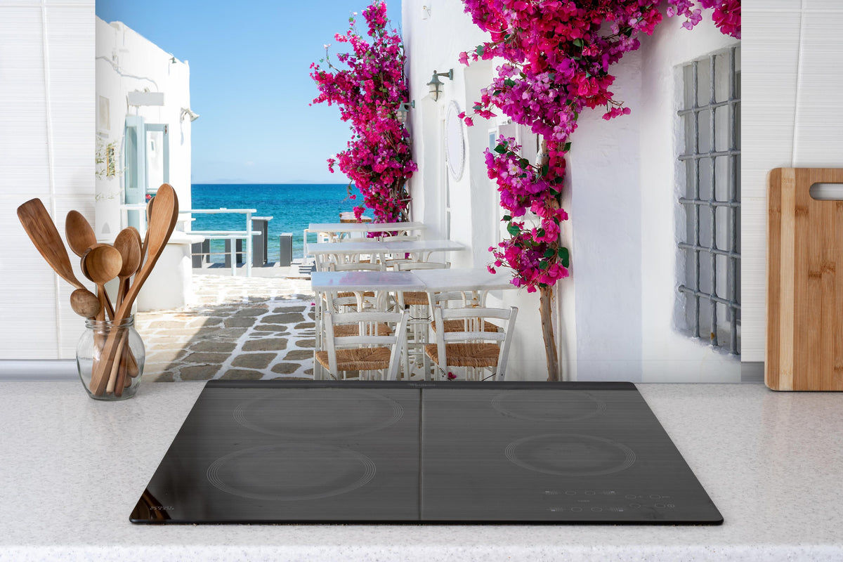 Spritzschutz - Weiße Gasse mit Oleander Blumen in Mykonos hinter einem Cerankochfeld zwischen Holz-Kochutensilien
